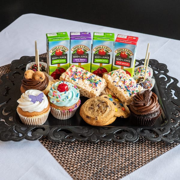 A black tray filled with cupcakes, cookies, Rice Krispies treats, cake pops, and juice boxes.