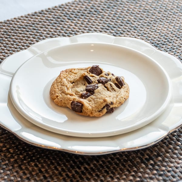 A single chocolate chip cookie on a small white plate, centered on a larger white plate.