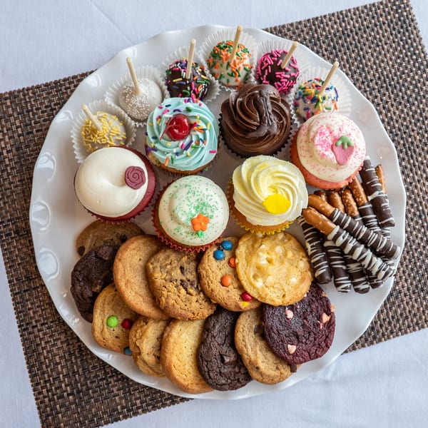 A white platter filled with an assortment of colorful cupcakes, cake pops, cookies, and chocolate-dipped pretzels.
