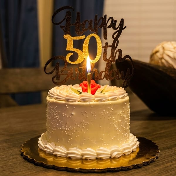 White birthday cake with sprinkles, a lit candle, and a "Happy 50th Birthday" topper.